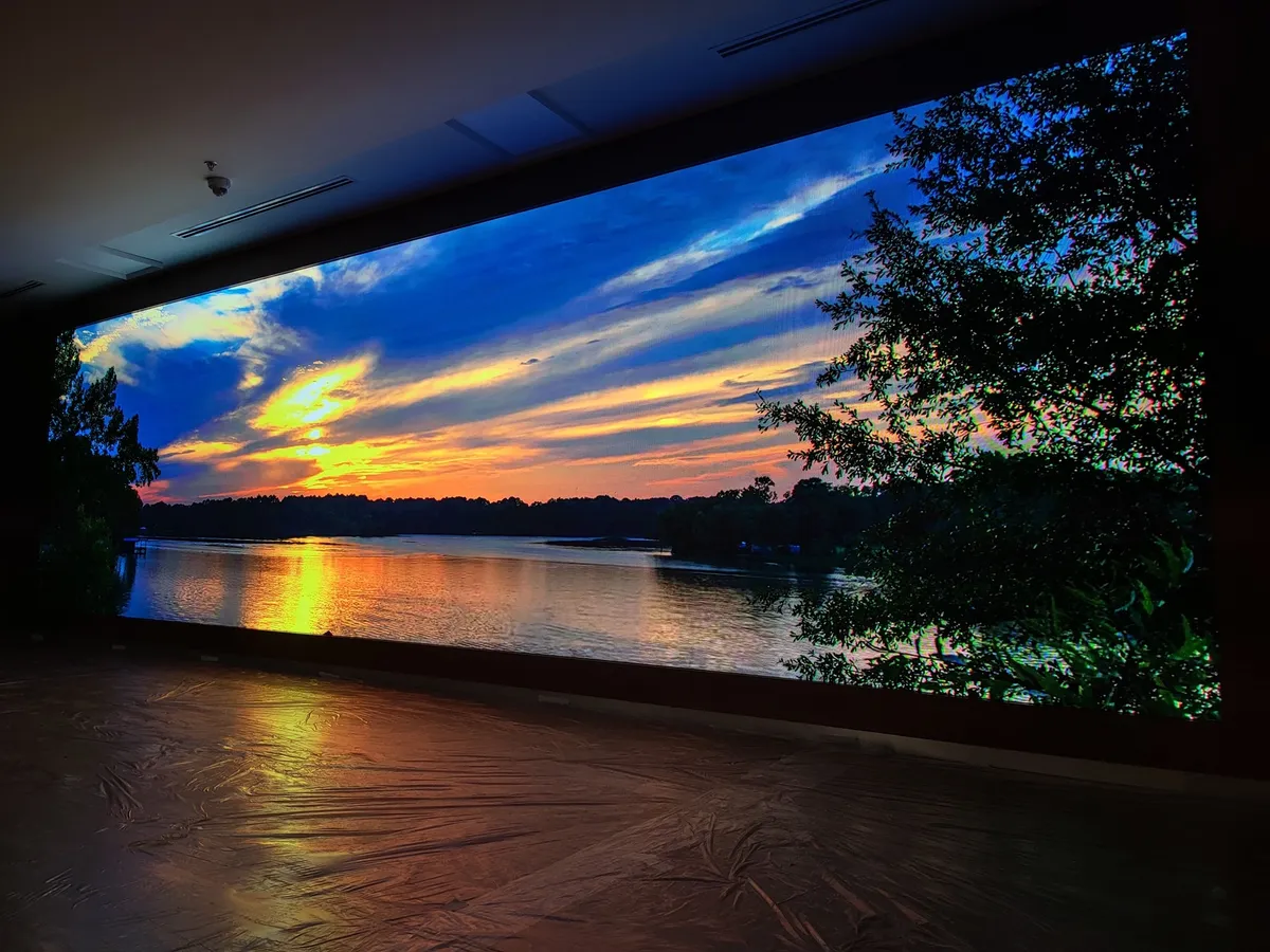 A large LED wall in the auditorium showing a sunset over a lake
