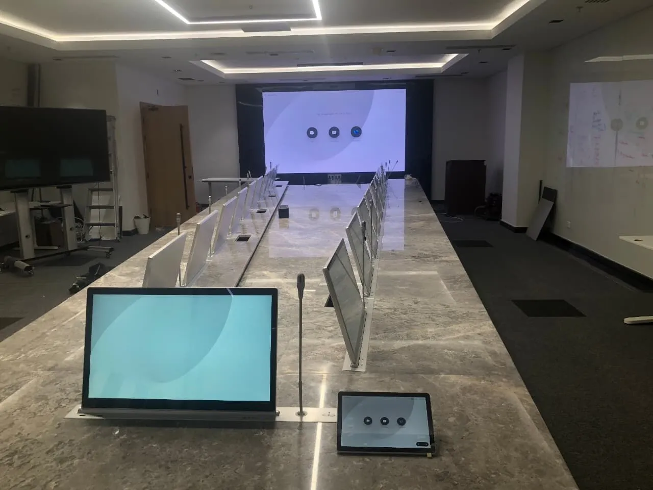 Boardroom with pop-up monitors along the table and a large screen at the end