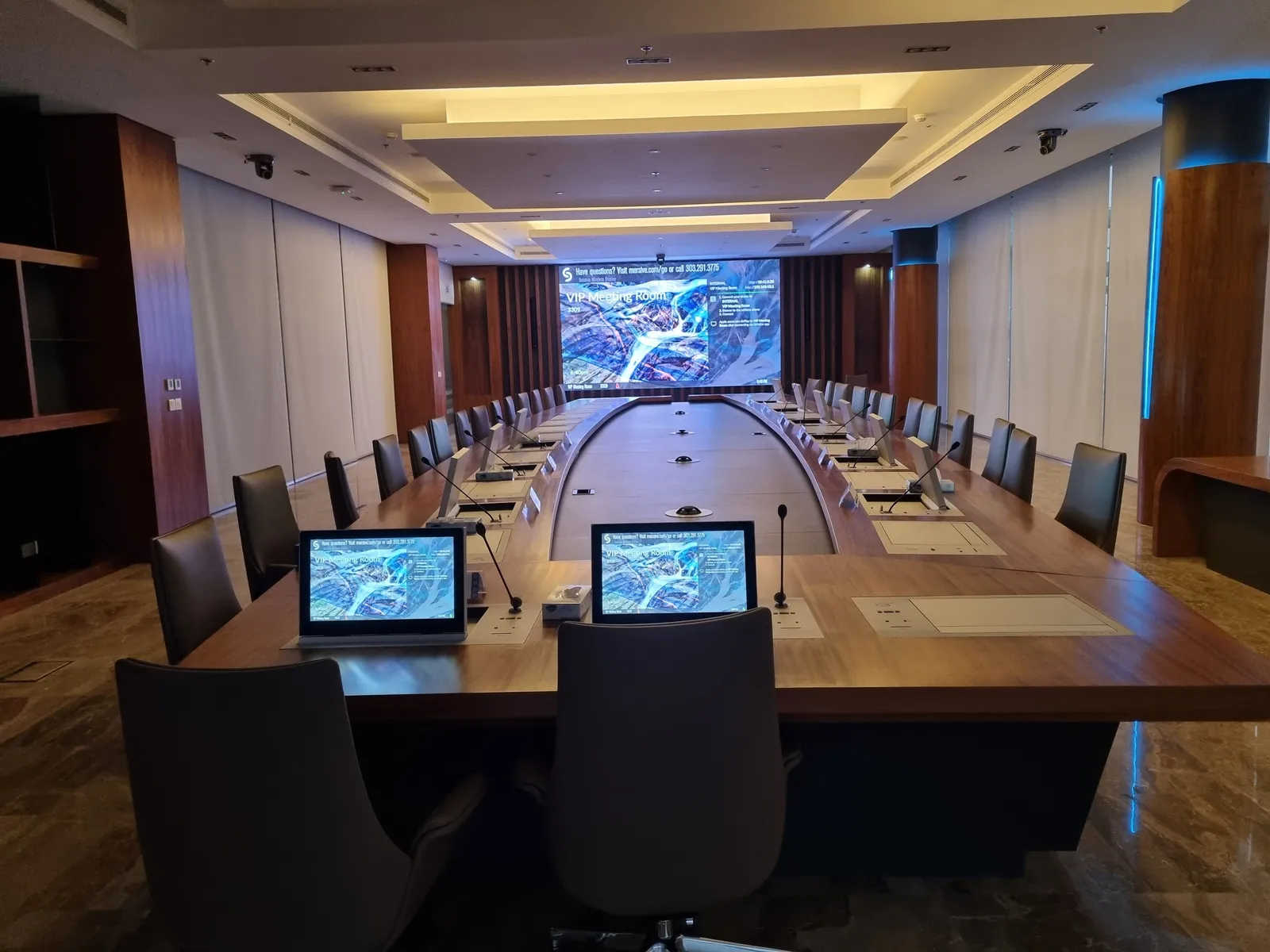 Board meeting room with a long table, lift-up monitors and an LED wall