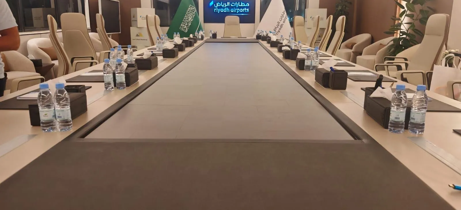 Long boardroom table with a Riyadh Airports screen at the far end